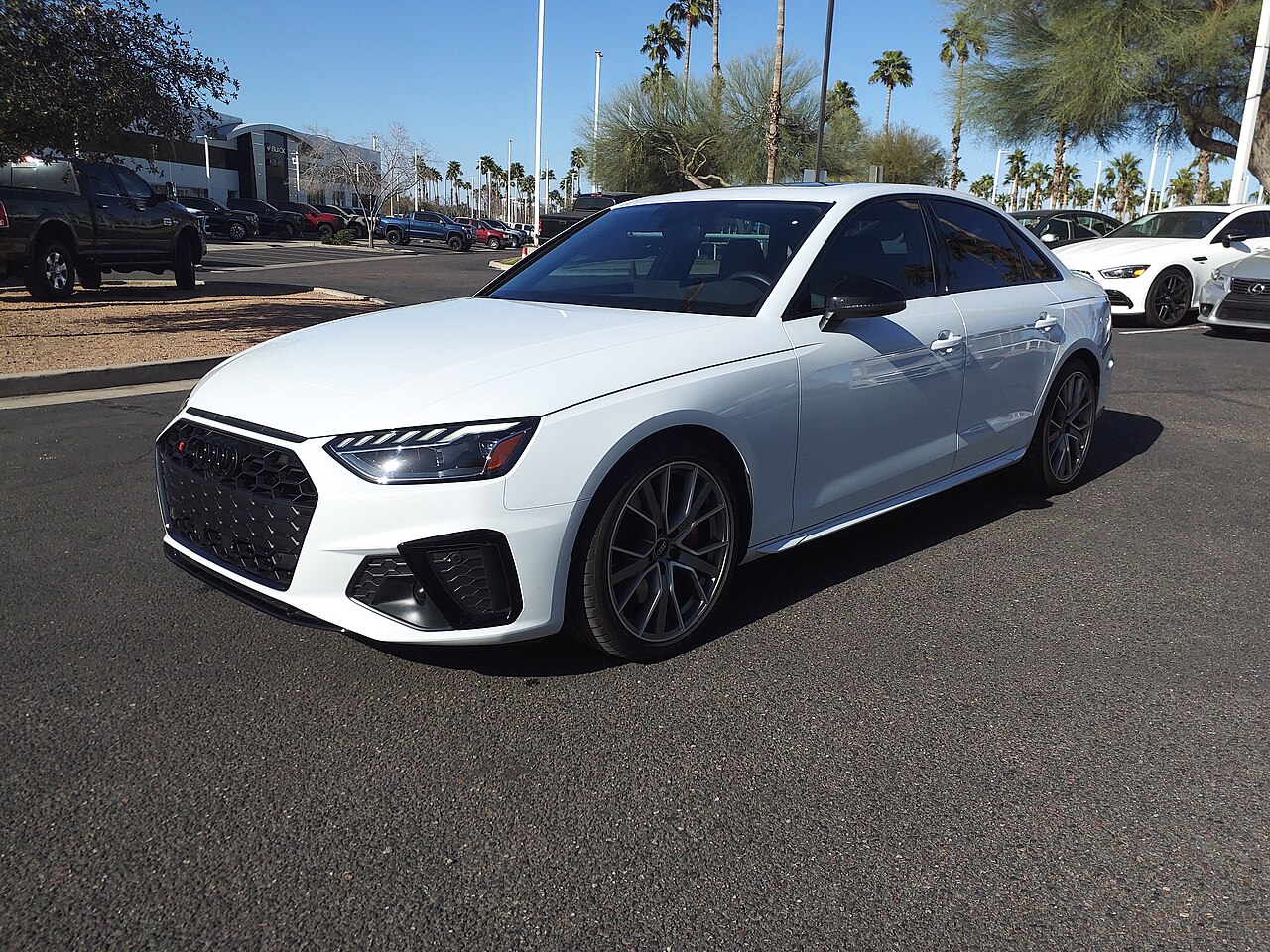 White Audi S4 B9 saloon with grey wheels, parked on a dealership lot with palm trees