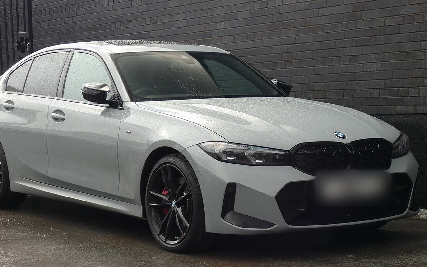 ‏BMW M340i G20 סדאן אפורה, אחרי פייסליפט, עם גריל כליות שחור וחישוקים שחורים, חונה ליד קיר לבנים