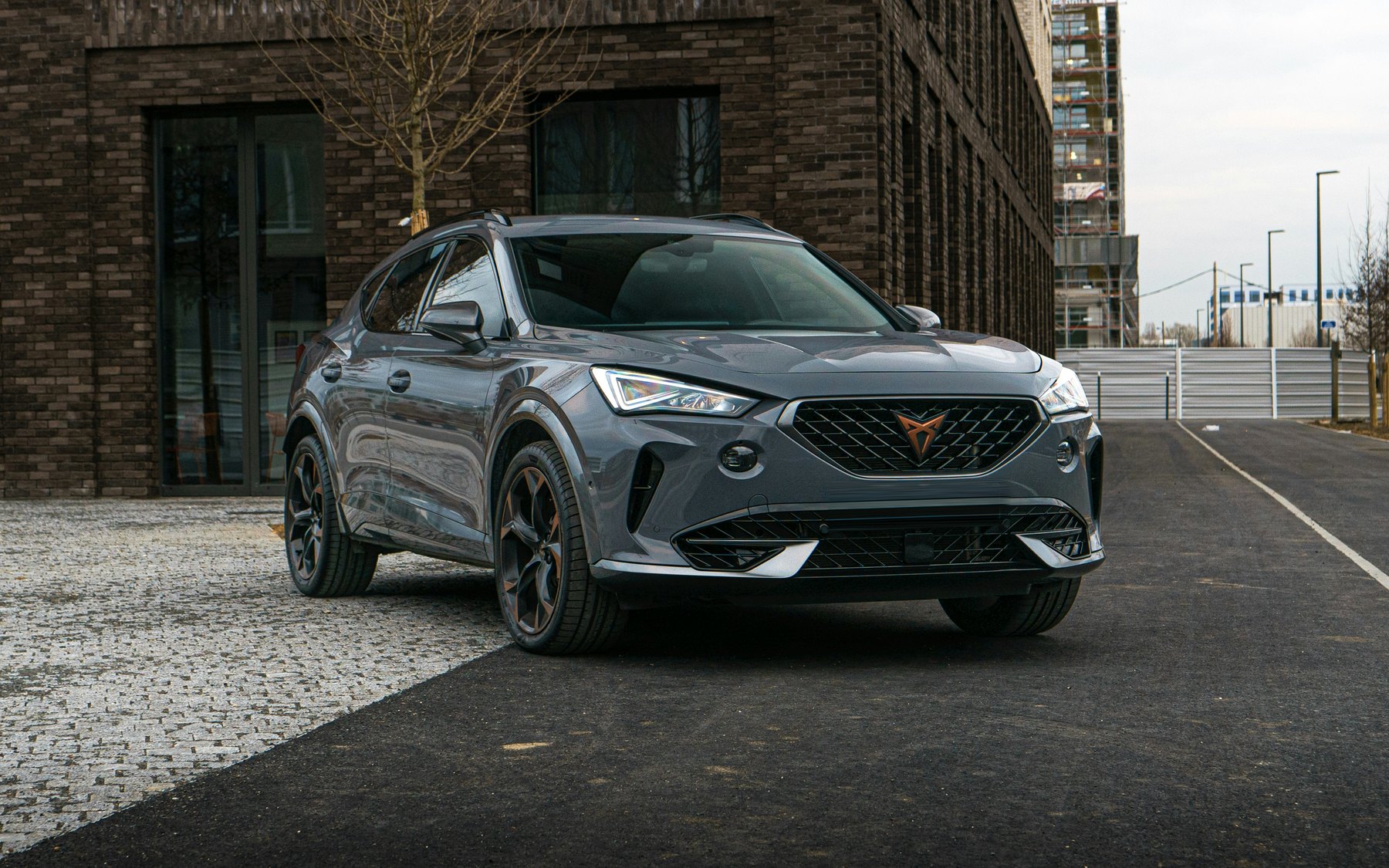 Grey Cupra Formentor VZ 2.0 TSI with the copper Cupra badge and VZ front bumper, parked in front of a brick building