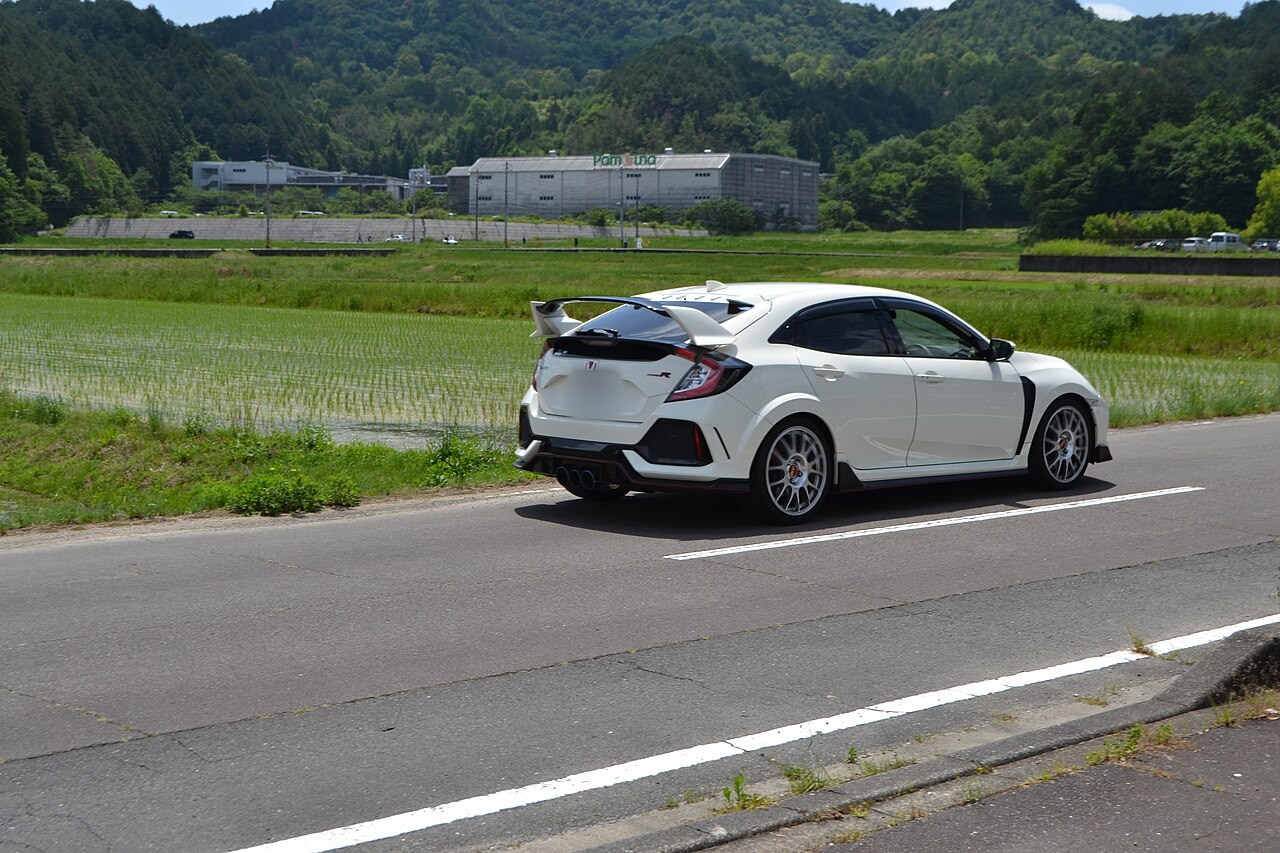 White Honda Civic Type R FK8 driving on a country road past rice fields, seen from the rear