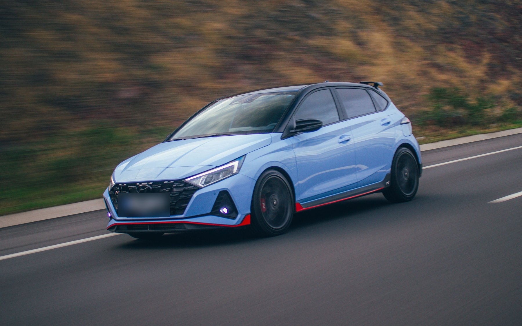 Performance Blue Hyundai i20 N with the N bumper and red lip, driving on a highway