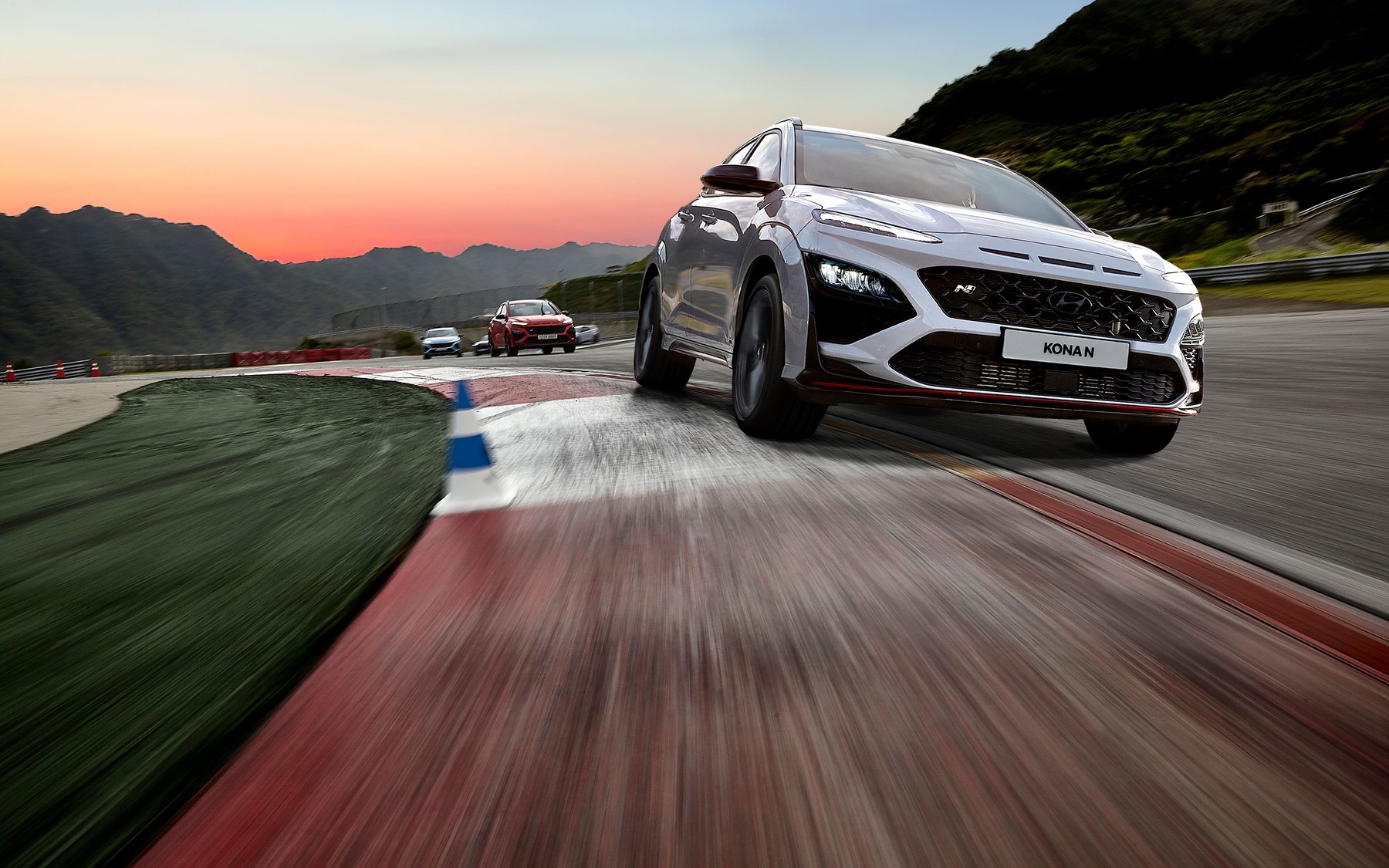 White Hyundai Kona N with the N grille badge and red lip, cornering on a race track at sunset