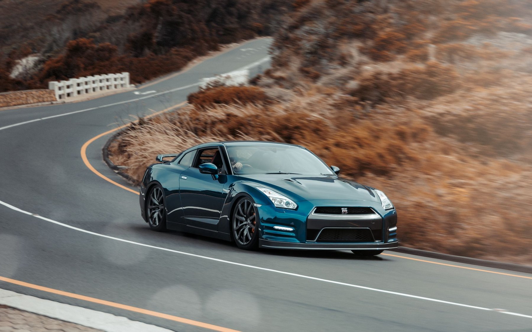 Teal Nissan GT-R R35 driving on a winding mountain road