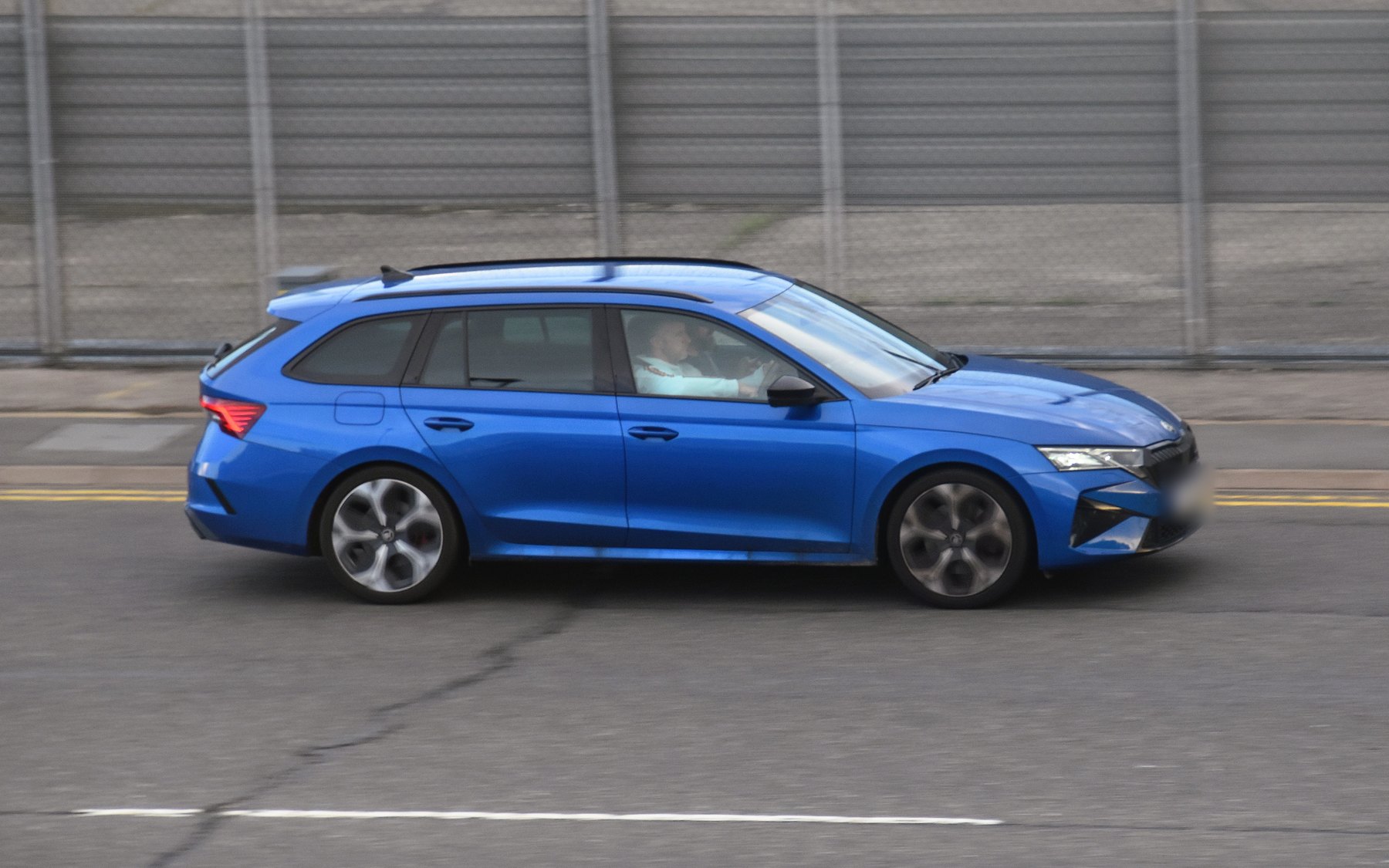 סקודה אוקטביה vRS קומבי 2.0 TSI כחולה, פייסליפט 2024, בנסיעה ליד גדר אפורה, מהצד