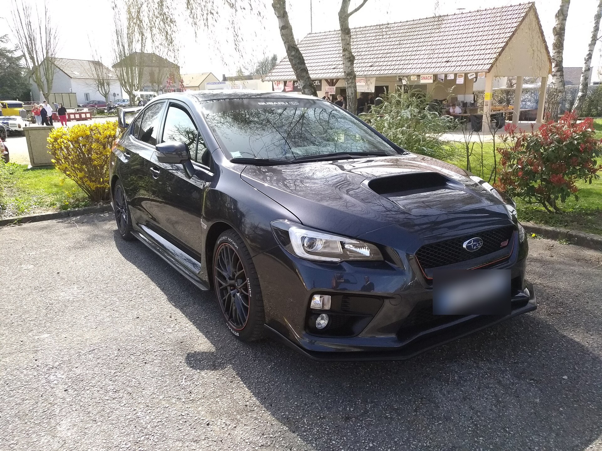 סובארו WRX STI ‏VA סדאן אפורה כהה עם חישוקים כהים, חונה ליד גינה