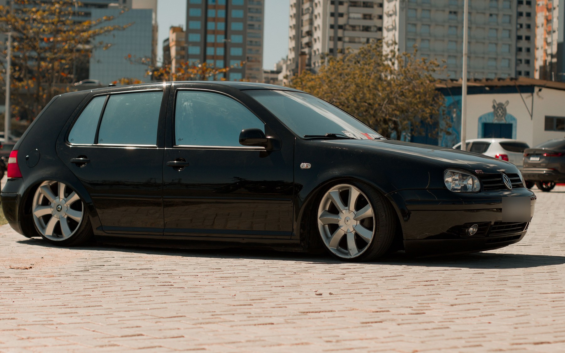 Black lowered VW Golf GTI Mk4 five-door with the GTI grille badge, parked on paving in a city