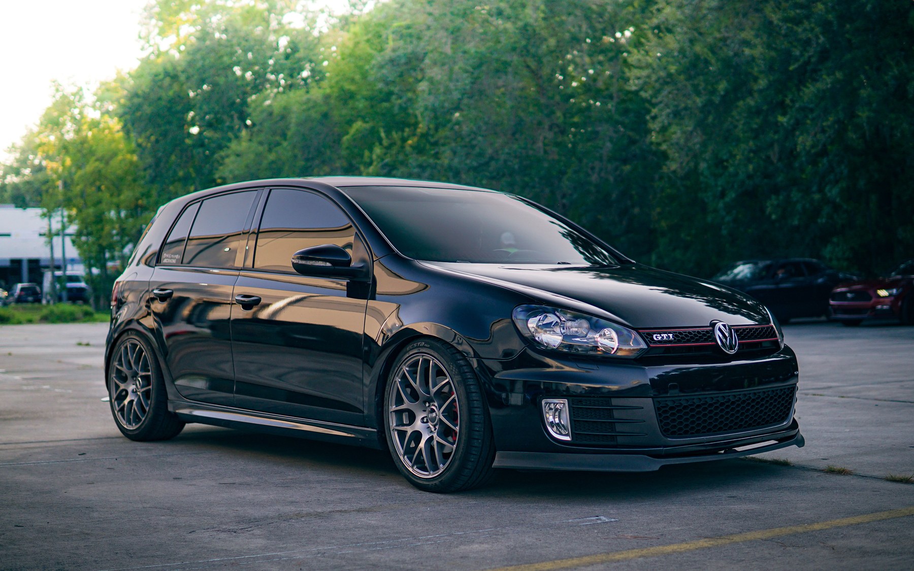 Black five-door VW Golf GTI Mk6 with the GTI badge and red grille stripes, parked in front of trees