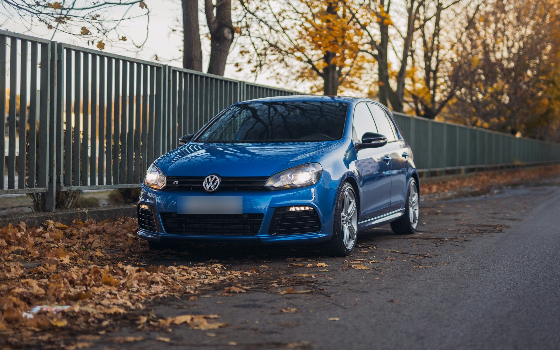 Blue five-door VW Golf R Mk6 with the R grille badge and R bumper, parked by a fence on an autumn street