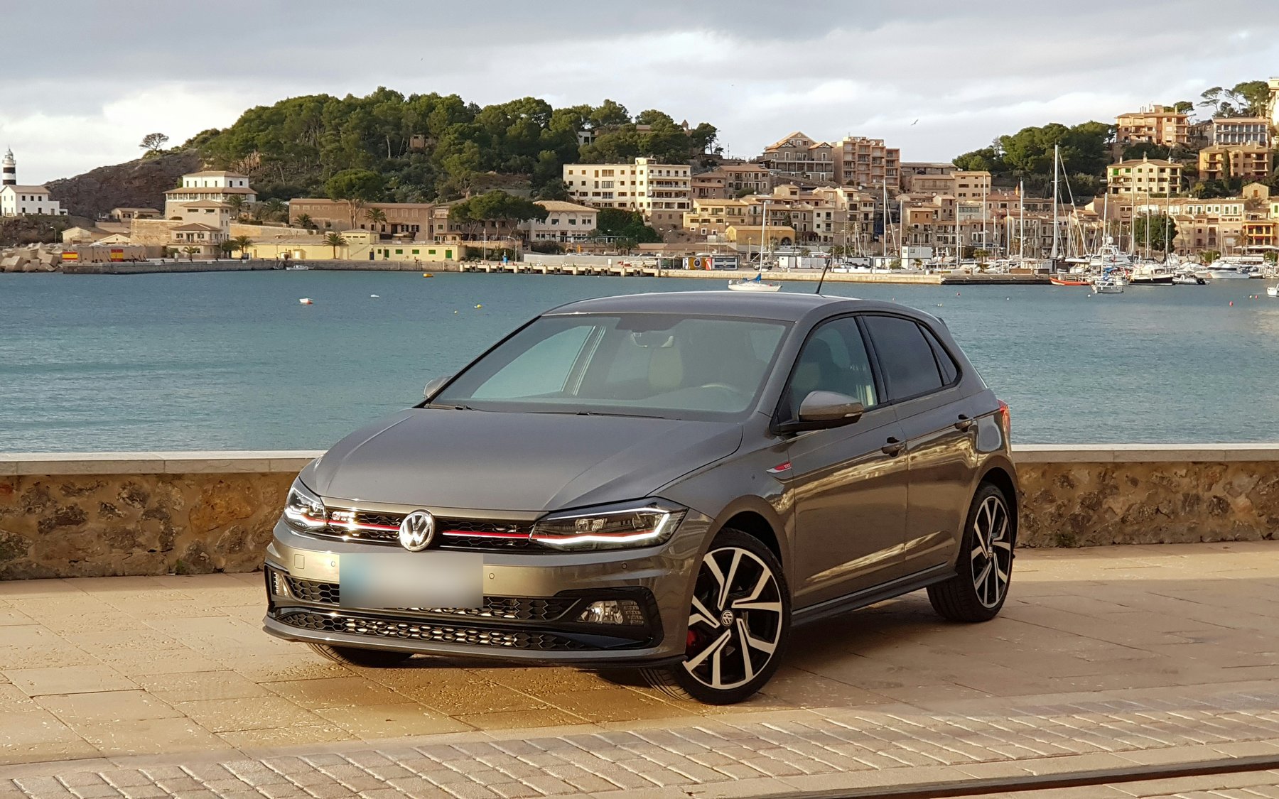 Grey VW Polo GTI Mk6 (AW) with the red grille stripe and GTI wheels, parked by a harbour