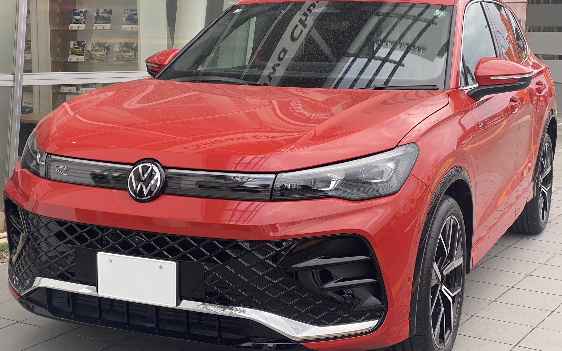 פולקסווגן טיגואן Mk3 eTSI R-Line אדומה, עם סמל R על פס האור לרוחב החזית ופגוש R-Line, חונה מול סוכנות
